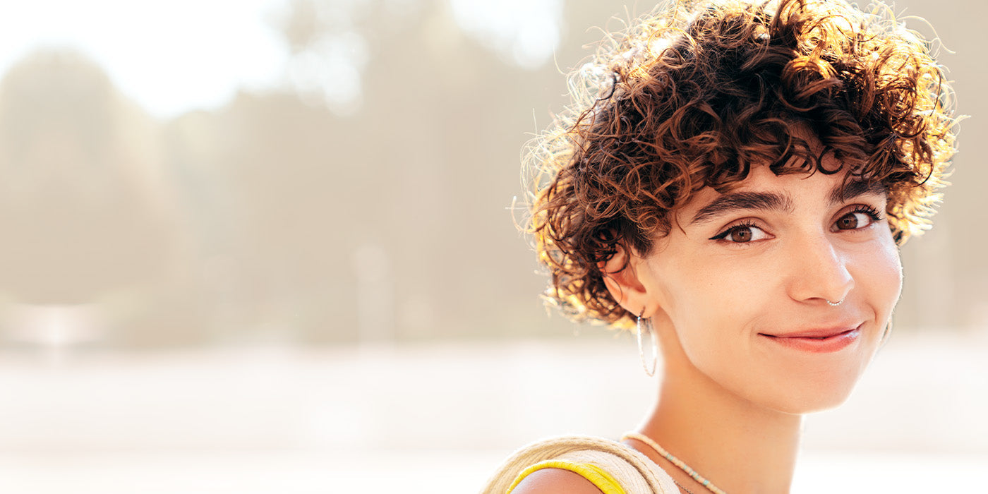 Junge Frau mit lockiger Kurzhaarfrisur und natürlichem Glow – frische Haarinspiration für den Spätsommer
