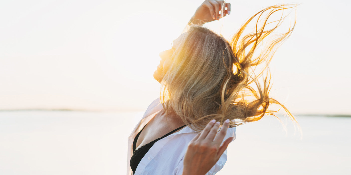 Frau mit wehenden blonden Haaren in der Sonne als Titelbild für Haarpflege nach den ersten warmen Tagen