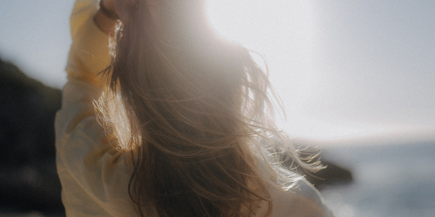 Frau mit langen Haaren in der Sonne, Haarstruktur wird vom Wind getragen – Sommermoment am Meer