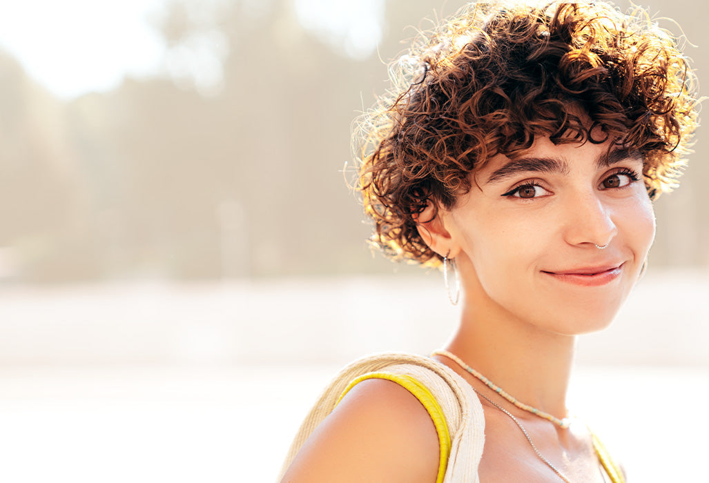 Junge Frau mit lockiger Kurzhaarfrisur und natürlichem Glow – frische Haarinspiration für den Spätsommer